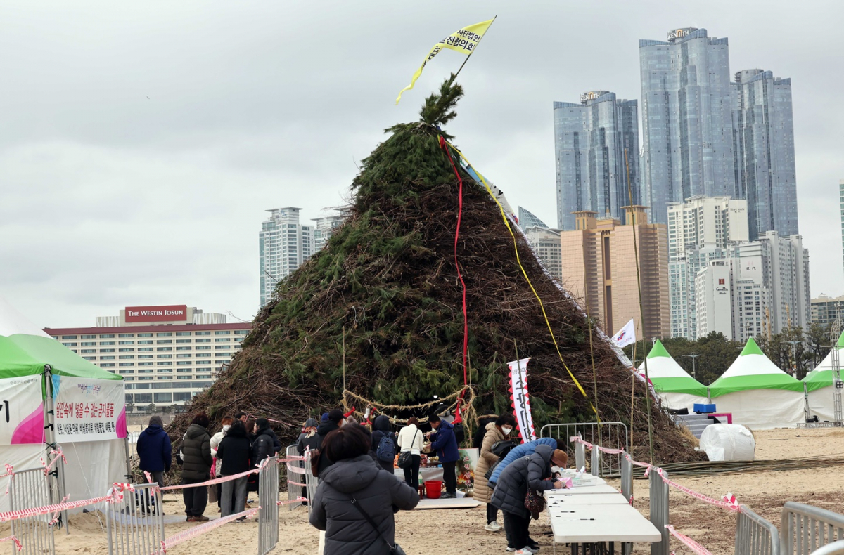 ▲ 정월대보름을 하루 앞둔 23일 부산 해운대구 해운대해수욕장을 찾은 시민들이 백사장에 조성된 대형 달집에 소망 기원문을 매달고 있다.  (뉴시스)