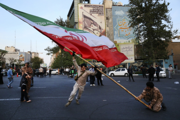 ▲15일(현지시간) 이란 테헤란의 팔레스타인 광장 건물벽에 걸린 반이스라엘 현수막 앞에서 시위대가 대형 이란 국기를 흔들고 있다.  (AP/뉴시스)