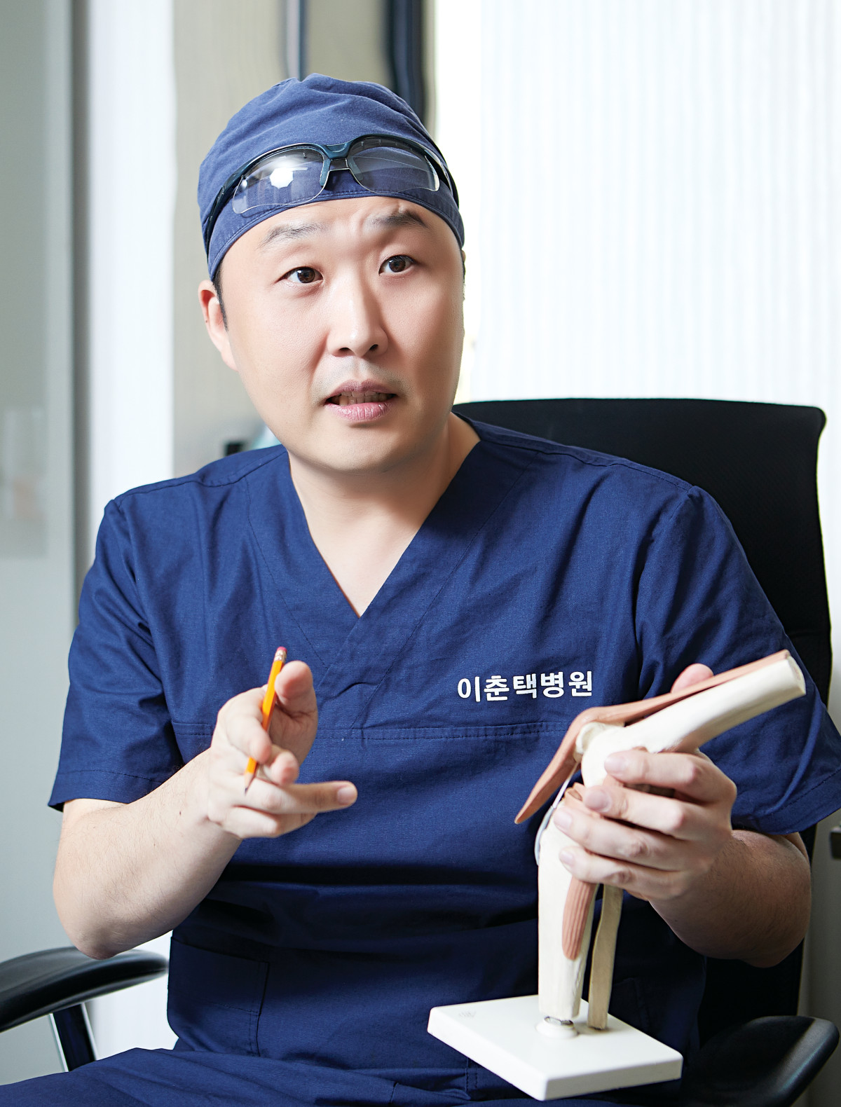 ▲이춘택병원의 윤성환 장산의료재단 수원 이춘택병원장이 수술복을 입고 무릎 관절 모형을 활용해 인공관절 수술에 대해 설명하고 있다. (이춘택병원)