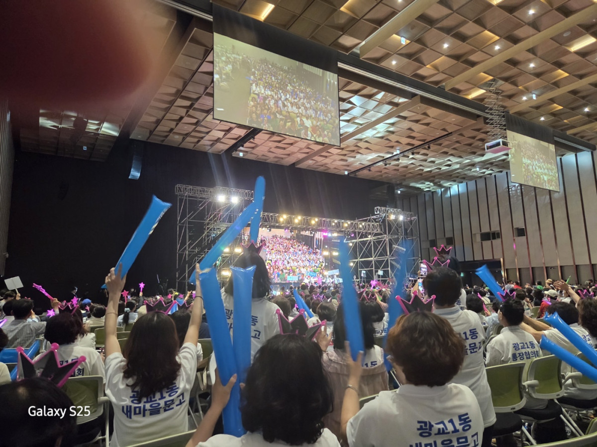 ▲13일 수원컨벤션센터에서 열린 ‘2025 새빛 힐링콘서트’에서 수원시 봉사자들이 단체 티셔츠와 핑크색 왕관 머리띠를 착용하고 파란 풍선을 흔들며 무대 공연을 관람하고 있다. (김재학 기자)