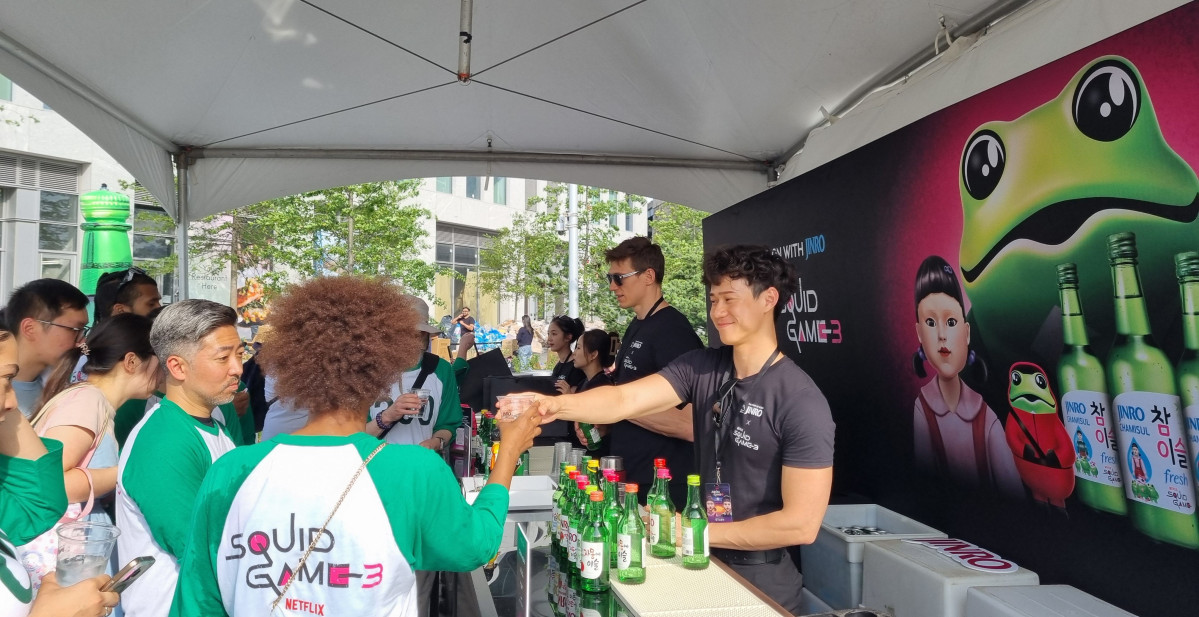 ▲오징어게임 컬래버 제품 출시와 관련해, 27일 행사장에서 'Squid Game' 문구가 적힌 옷을 입은 사람들이 소주 병이 진열된 테이블 앞에서 프로모션에 참여하고 있다. (사진제공=하이트진로)