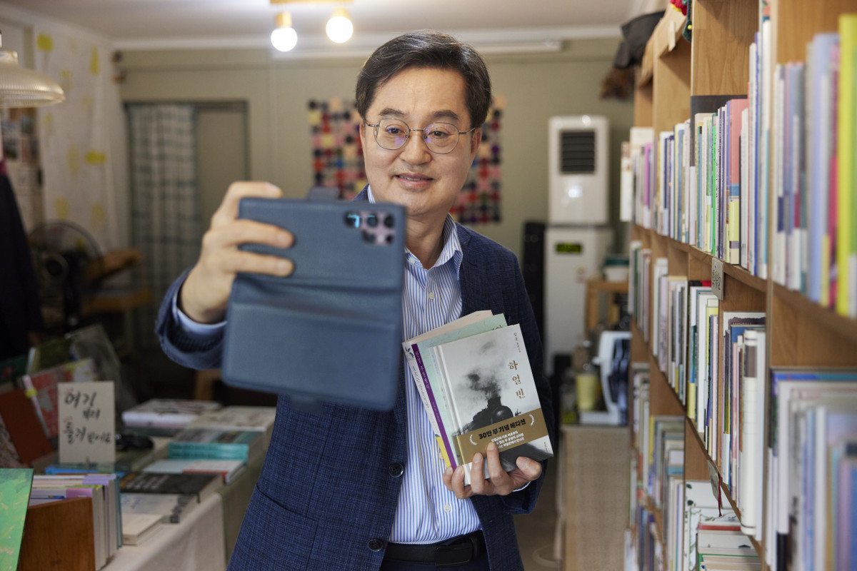 ▲김동연 경기도지사가 29일 수원 장안구 광화문서림에서 여름휴가때 읽을 책을 들고 스마트폰으로 사진을 찍고 있다. (경기도)