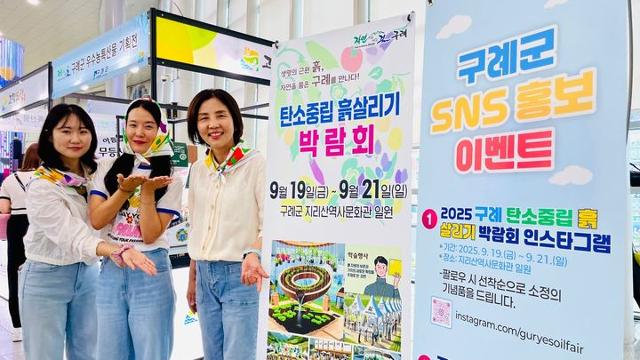▲9월 19일부터 개최되는 '2025 구례 탄소중립 흙 살리기 박람회'를 앞두고, 관계자들이 박람회 홍보 배너 앞에서 시민들에게 행사를 알리고 있다. (사진제공=구례군)