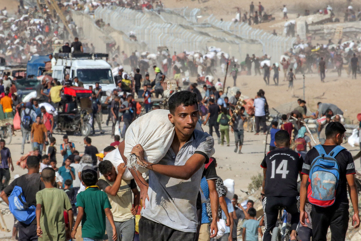 ▲미국과 이스라엘의 지원을 받는 가자 인도주의 재단(GHF)이 운영하는 물류 센터에서 한 청년이 인도주의적 지원을 받은 가방을 들고 어깨에 자루를 메고 걷고 있다. AFP연합뉴스