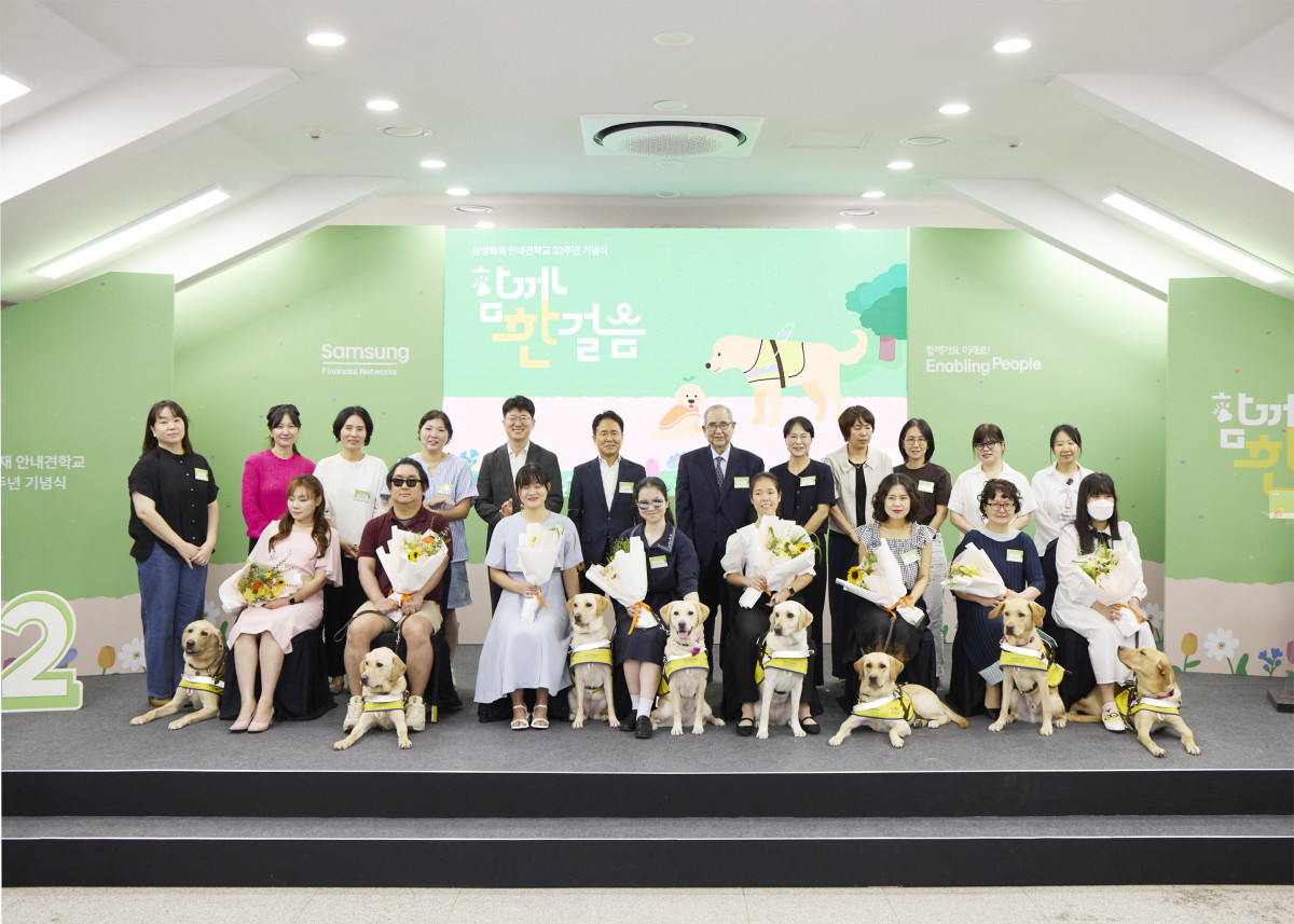 ▲8월 26일 용인 삼성화재 안내견학교에서 열린 32주년 기념식에서 안내견을 분양 받은 파트너들과 행사에 참여한 내빈들이 기념촬영을 하고 있다. (삼성화재 제공)