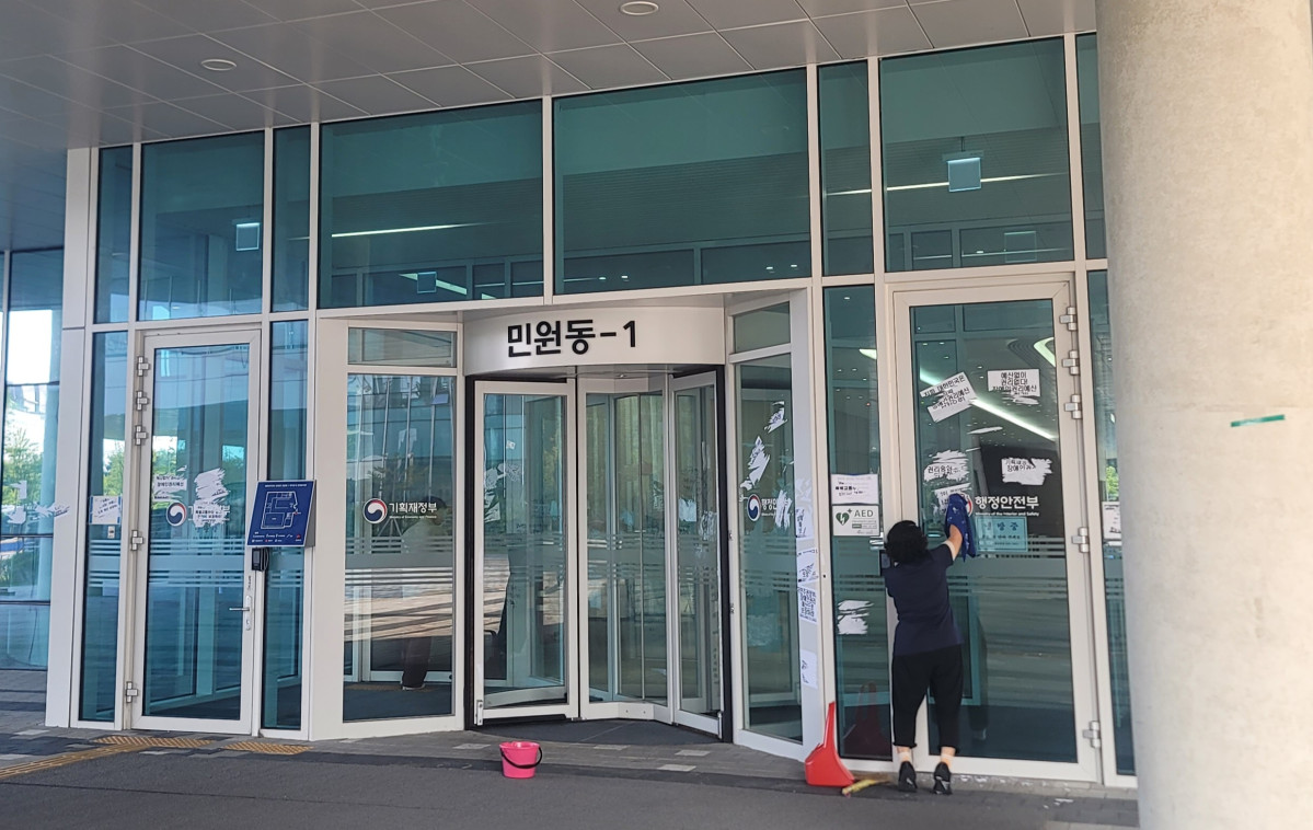 ▲28일 정부세종청사 민원동 앞에서 한 환경실무원이 전국장애인차별철폐연대(전장연)가 26~27일 기획재정부에 '장애인 권리예산 보장'을 촉구하는 시위 과정에서 해당 건물에 붙인 스티커를 닦아내고 있다. (정호영 기자)