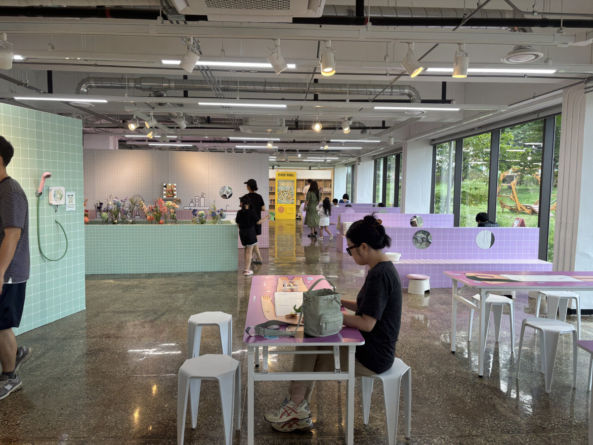 ▲경기상상캠퍼스에서 관람객들이 연한 파란색과 보라색 타일로 꾸며진 전시 공간 내 테이블에서 활동을 하고 있다. (경기문화재단)