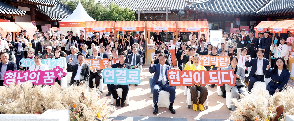 ▲제2회 청년창업박람회가 열린 전주 한옥마을 일원에서 참가자들이 야외 행사에 모여 창업 응원 문구가 적힌 팻말을 들고 있다. (사진제공=전북도)