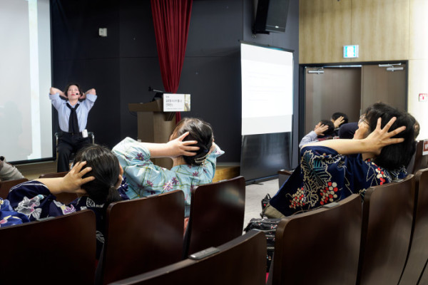 ▲페이스 짐 체험 프로그램에서 관람객들이 강사의 안내에 따라 앉은 자세로 얼굴·두피를 자극하는 동작을 따라 하고 있다. 현장에는 기모노 차림의 일본 참가자도 함께 참여해 국제 행사 분위기를 더했다.(이준호 기자)