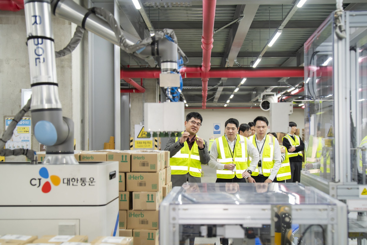 ▲CJ대한통운 인천 GDC를 방문한 태국 최대 유통사 CP 엑스트라 경영진들이 박스를 자동 분류해 파렛트에 쌓는 '이동형 로봇 팔레타이저'에 대해 설명을 듣고 있다. (사진=CJ대한통운)