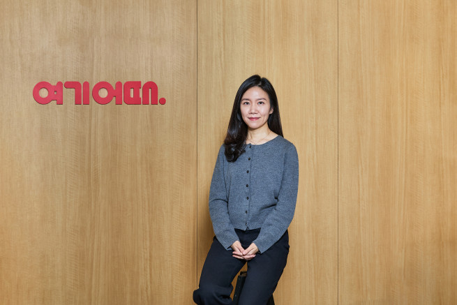 ▲김승미 여기어때 패키지TF 실장이 회사 로고 앞에서 포즈를 취하고 있다. (사진제공=여기어때)