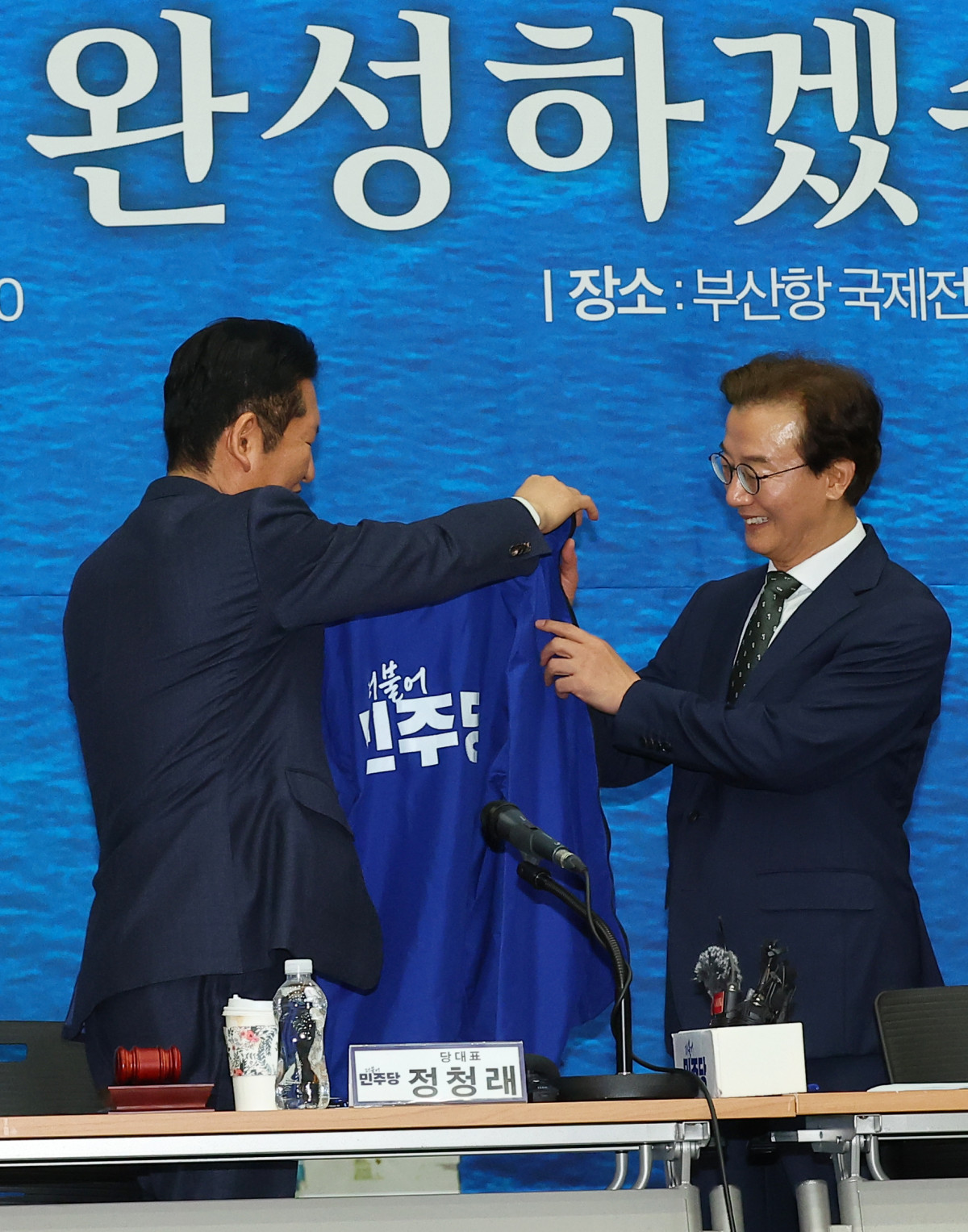 ▲더불어민주당 정청래 대표가 15일 오전 부산 동구 부산항국제전시컨벤션센터에서 열린 부산 현장 최고위원회에서 전재수 부산시장 후보에게 파란 점퍼를 입혀주고 있다. (사진=연합뉴스)