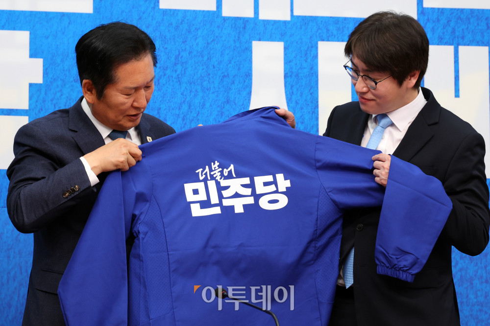 ▲하정우(오른쪽) 전 청와대 AI수석이 29일 서울 여의도 국회에서 열린 민주당 인재영입식에서 정청래 당대표에게 파란 점퍼를 받고 있다. 고이란 기자 photoeran@