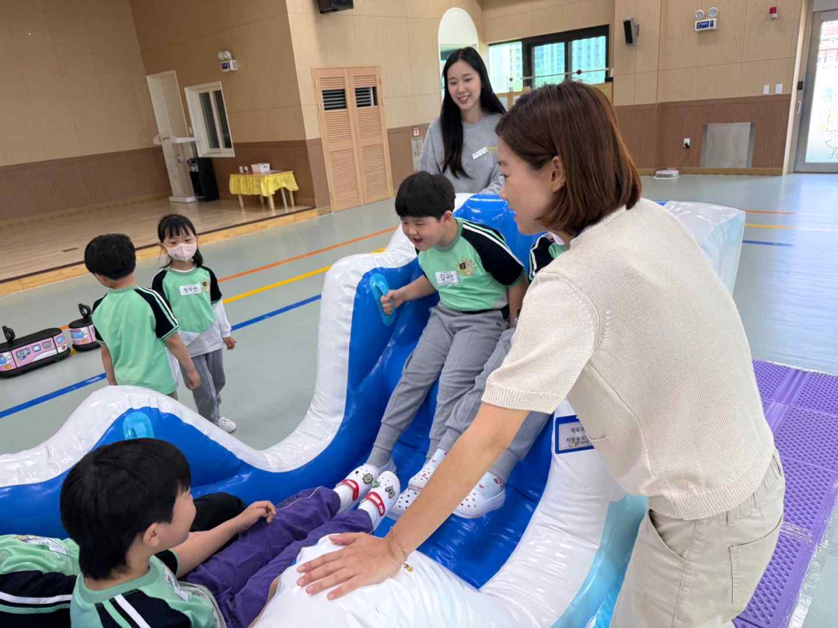 ▲강당에서 진행된 에어바운스 놀이에서 학부모 자원봉사자가 미끄럼을 타고 내려오는 유아를 두 손으로 안전하게 받쳐주고 있다. 이날 행사는 학부모회의 적극적인 참여로 유아·교사·학부모가 하나 된 교육공동체의 모습을 보여줬다. (물빛나래유치원)