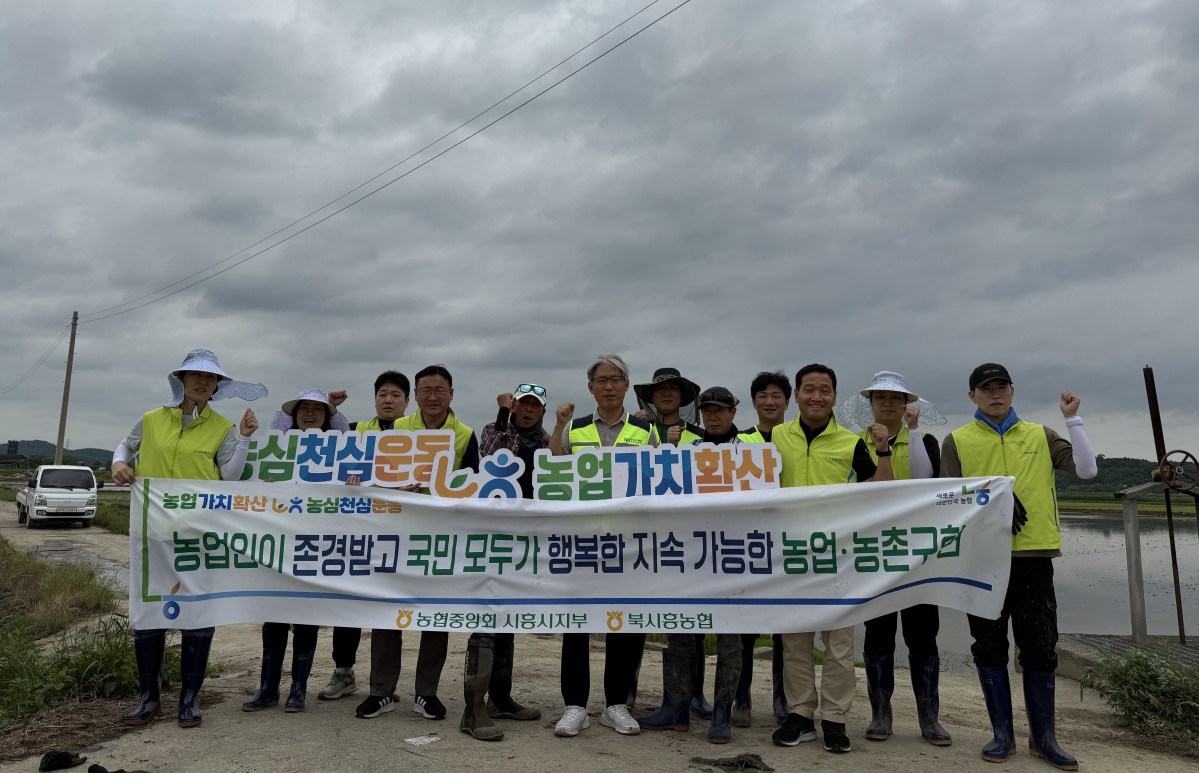 ▲농협중앙회 시흥시지부와 농협은행 고객행복센터 직원들이 27일 시흥시 하중동 농가에서 영농철 모내기 일손돕기를 마친 뒤 '농심천심 운동·농업 가치 확산' 현수막을 펼치고 기념촬영을 하고 있다. (경기농협)