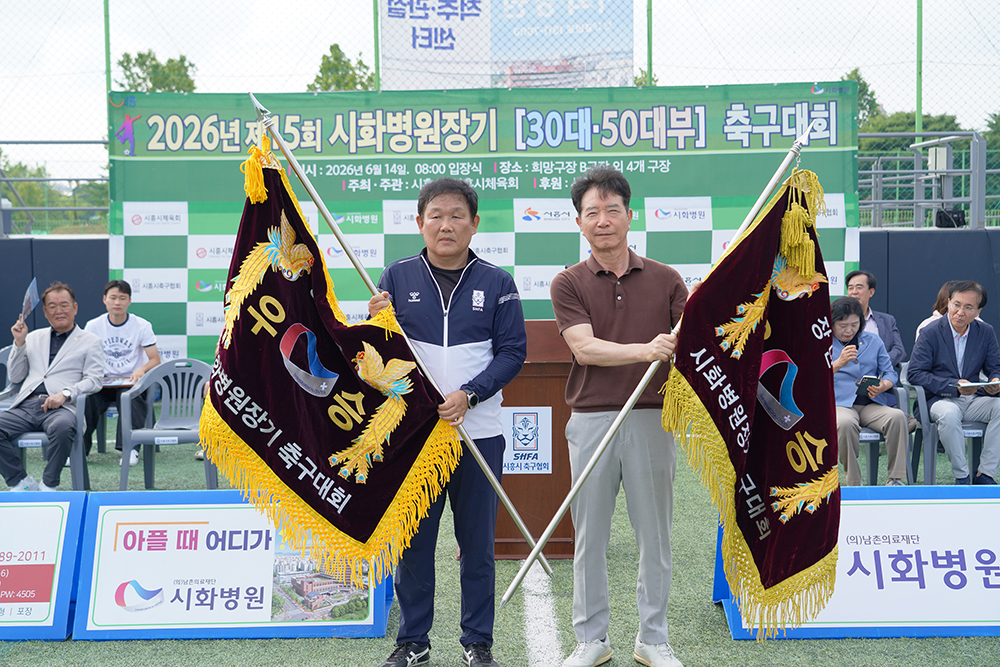 ▲장관구 시흥시축구협회장(왼쪽)과 최병철 시화병원 이사장이 21일 희망구장에서 열린 '제15회 시화병원장기 축구대회' 시상식에서 우승기를 들어 보이고 있다. 이번 대회에는 30대부 18개 팀과 50대부 20개 팀 등 총 38개 팀이 참가했다. (시화병원)