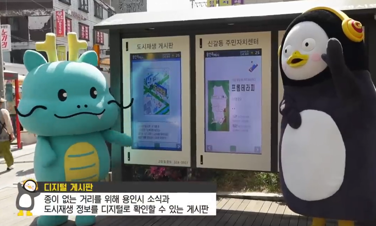 ▲용인특례시 캐릭터 조아용과 EBS 캐릭터 펭수가 함께한 신갈오거리 스마트 도시재생 홍보 영상의 한 장면. 종이 없는 거리를 위해 용인시 소식과 도시재생 정보를 디지털로 확인할 수 있는 디지털 게시판을 소개하고 있다. (용인특례시)