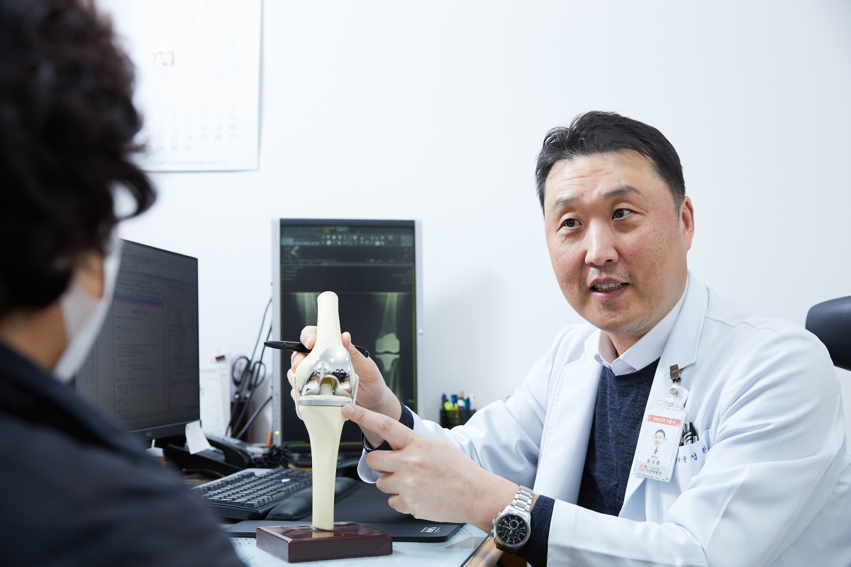 ▲윤성환 이춘택병원장이 진료실에서 무릎 인공관절 모형을 들고 환자에게 수술 과정과 치료 방향을 설명하고 있다. 윤 병원장은 "기술은 환자의 치료 결과를 높이기 위한 수단이어야 한다"는 철학으로 환자 중심 진료를 실천하고 있다. (이춘택병원)