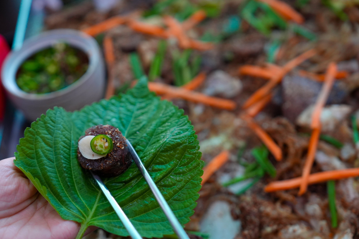 ▲원 지동시장 순대타운에서 손님이 순대를 깻잎에 올려 맛보고 있다. (수원특례시)
