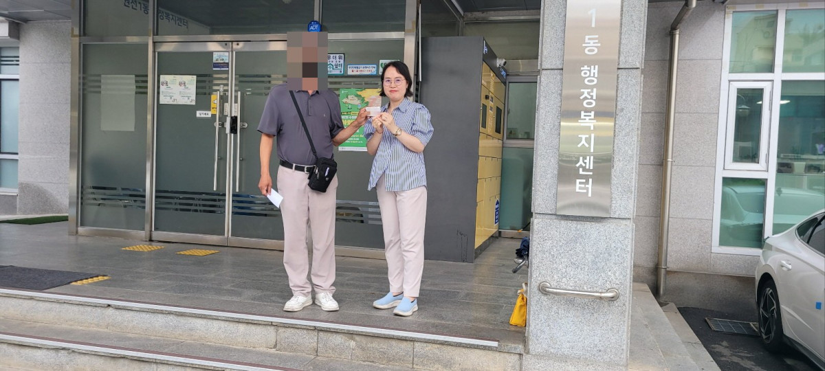 ▲60여 년 만에 주민등록증을 발급받은 강모 씨가 6월 동행정복지센터 앞에서 김경숙 수원시 새빛민원실 베테랑팀장과 함께 주민등록증을 들어 보이고 있다. (수원특례시)