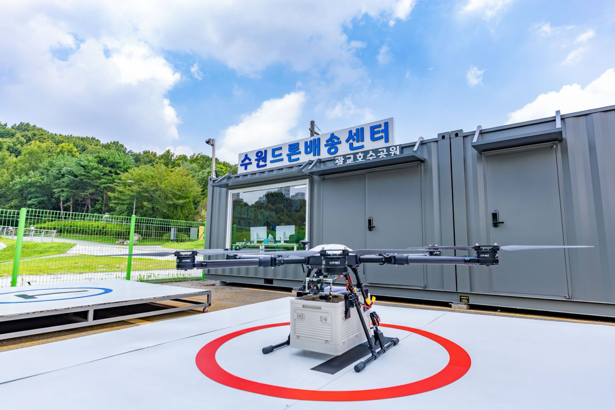 ▲수원시가 광교호수공원에 설치한 수원드론배송센터 앞 이착륙장에 배송용 드론이 물품 상자를 싣고 대기하고 있다. 수원시는 8월부터 11월까지 매주 주말 광교호수공원과 광교저수지에서 드론 배송을 시범 운영한다. (이재준 수원특례시장 페이스북)