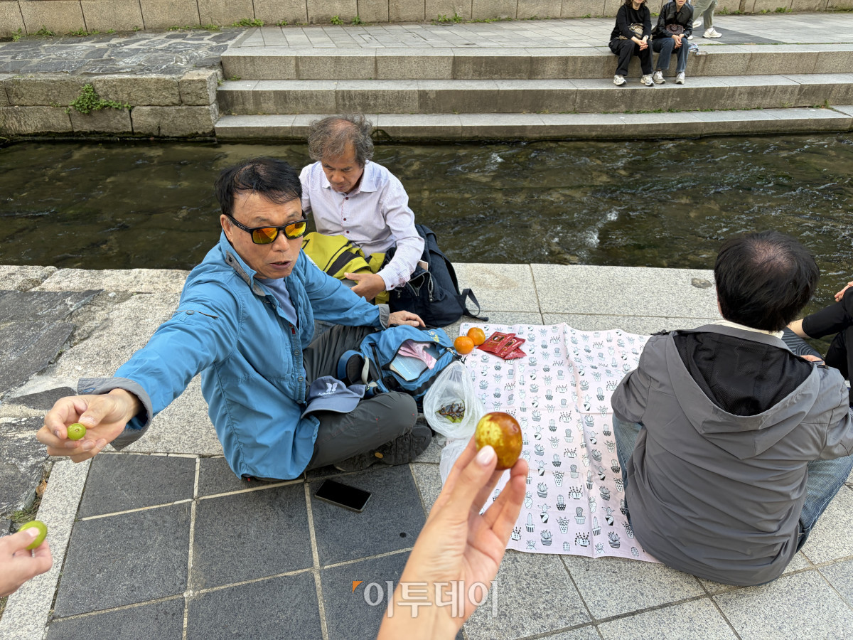 ▲6일 오후 서울 중구 청계천에서 분홍색 돗자리를 펴고 가을 나들이를 즐기고 있는 시민들이 본지 수습기자에게 샤인머스캣 한 알을 건네주고 있다. 김주리 수습기자 juri@