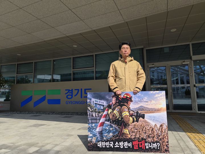 ▲윤성근 전 경기도의원이 16일 수원시 영통구 경기도청 앞에서 '대한민국 소방관이 빨대입니까?'라고 적힌 피켓을 들고 1인 시위를 하고 있다. (뉴시스)